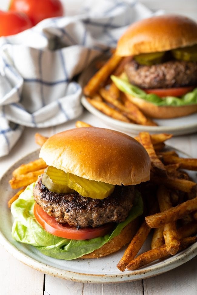 A gourmet hamburger with a brioche bun, avocado, bacon, and a fried egg, served with sweet potato fries