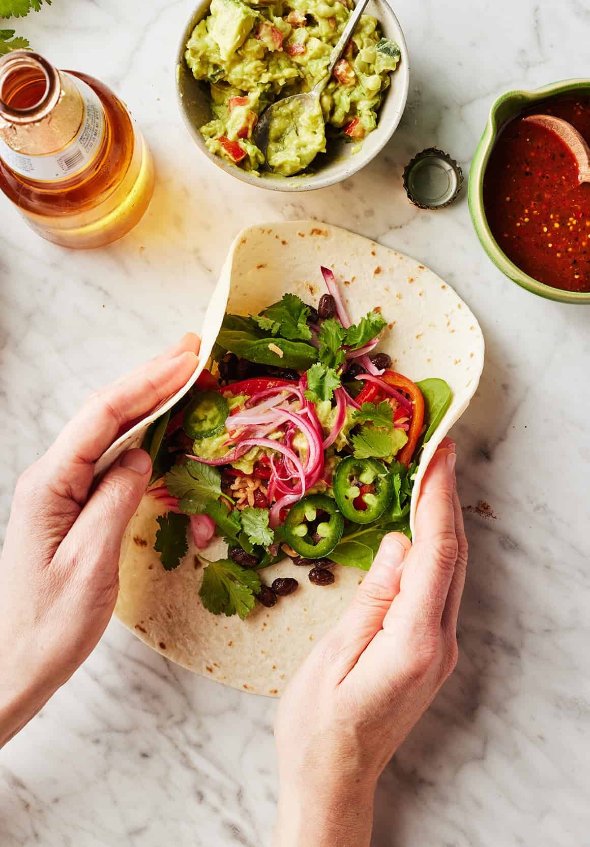 Hands folding sides of tortilla over burrito filling