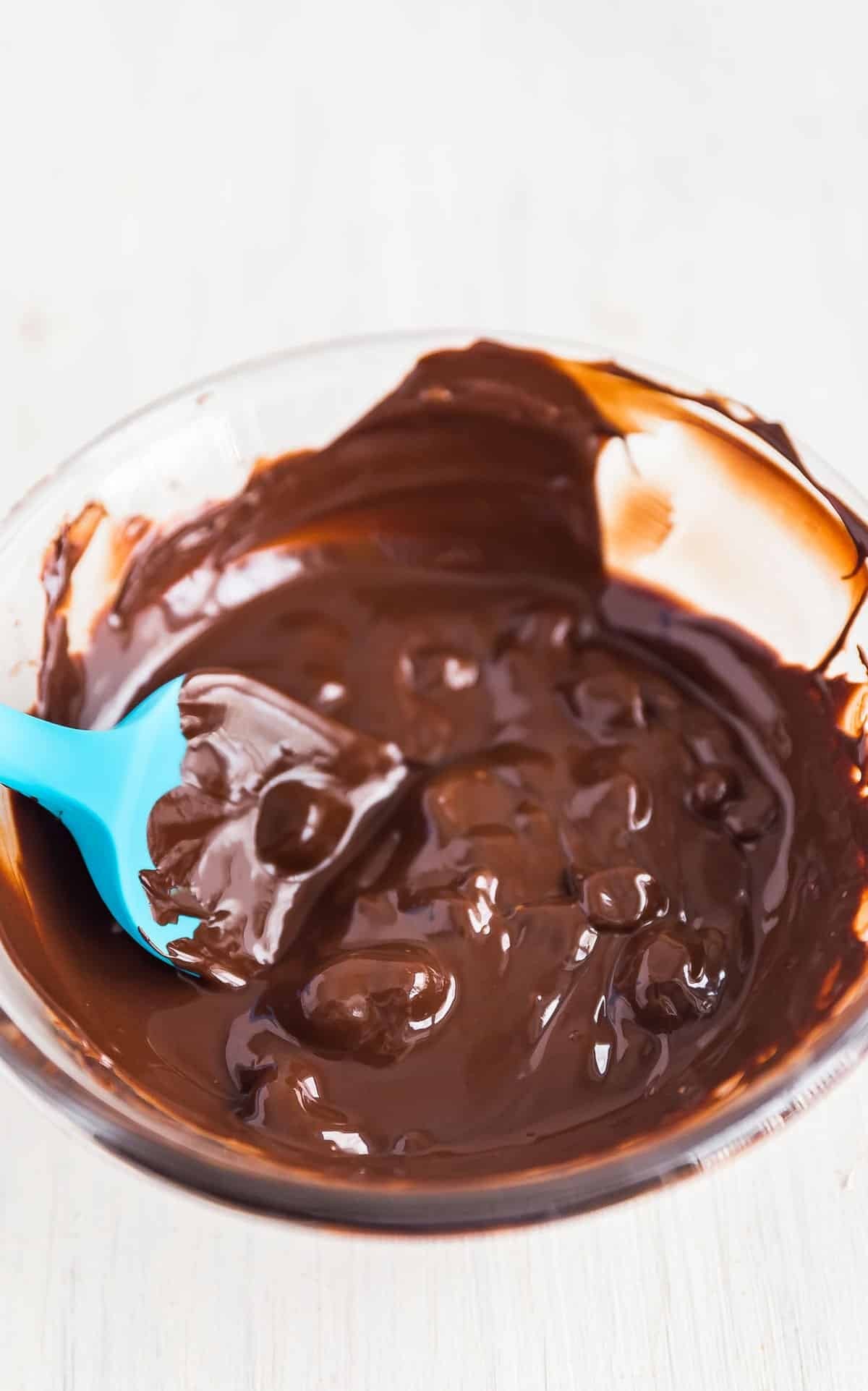 Microwaved chocolate chips in a glass bowl, mostly melted with a few solid pieces remaining, ready for the final stir.