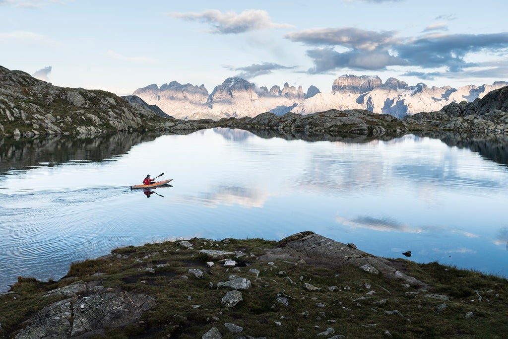 person paddling a kayak on a crystal clear alpine lake
