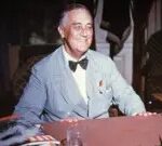 Franklin Delano Roosevelt seated at his desk, smiling