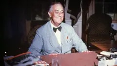 Franklin Delano Roosevelt seated at his desk, smiling