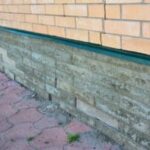 Exterior foundation damage and water pooling near a house.