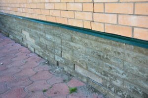 Exterior foundation damage and water pooling near a house.