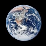 A view of Earth from Apollo 17 showing the blue ocean, reddish brown landmasses, and wispy, white clouds.