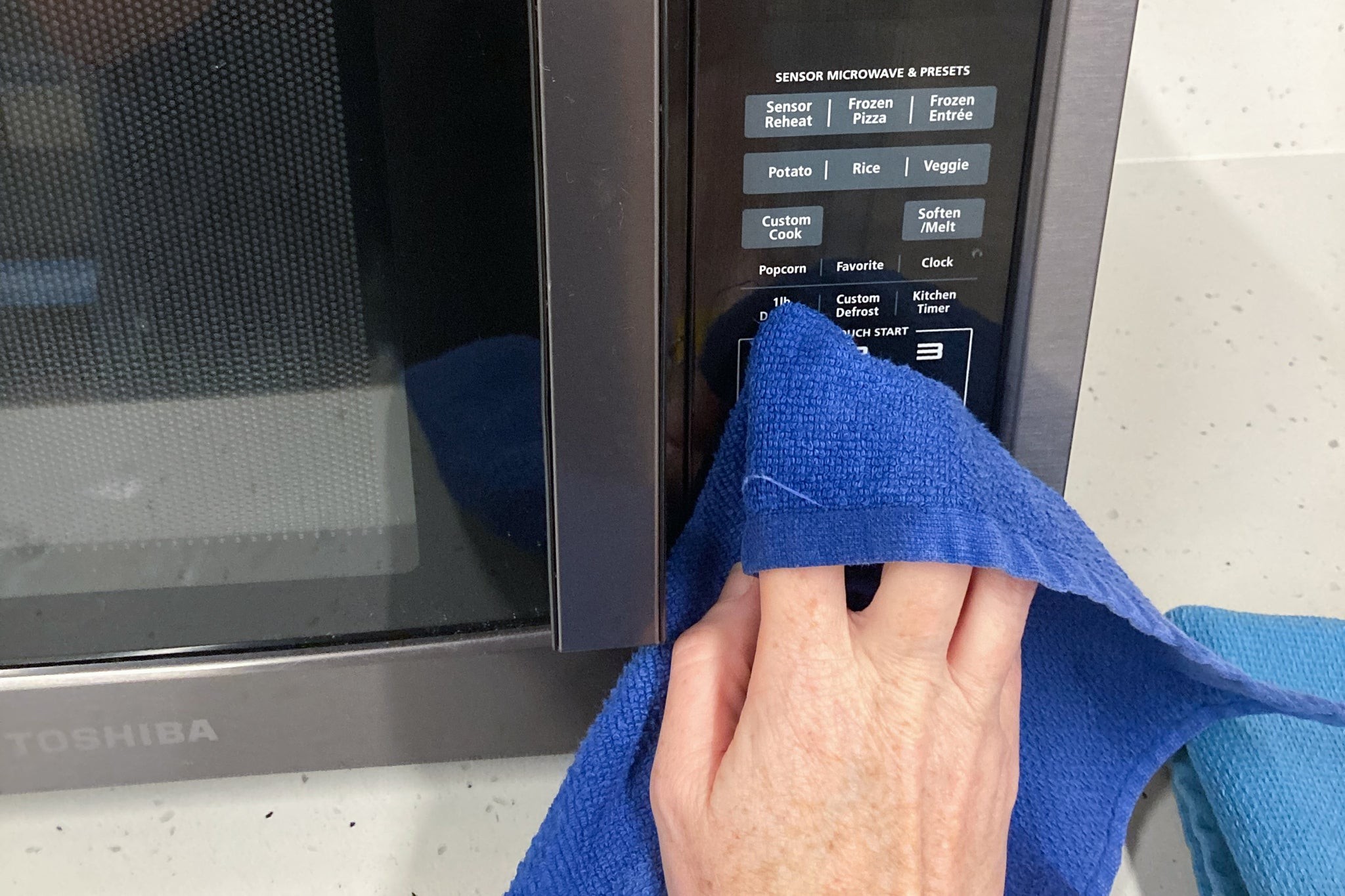 A person wiping down the outside of a microwave with a microfiber cloth.