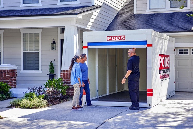 A PODS driver has just delivered a PODS portable storage container to a residential driveway. He has opened the container door and is showing the inside to a mature couple who will be using it for storage.