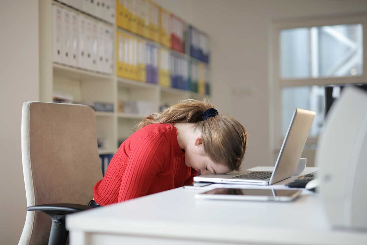 A person asleep at their desk with their head on their arms