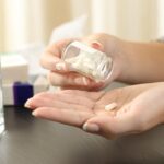 Close up of a woman taking a pill from bottle on a table