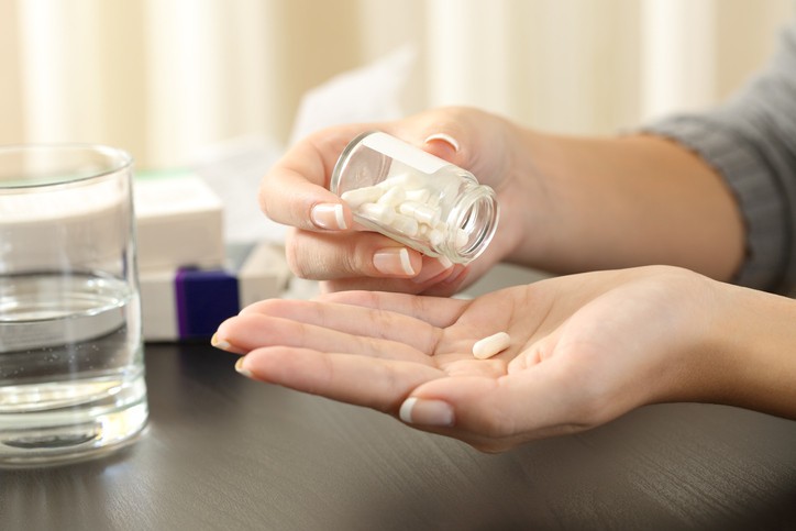 Close up of a woman taking a pill from bottle on a table