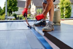 Man working on a flat roof, potentially inspecting it for repair or replacement needs.
