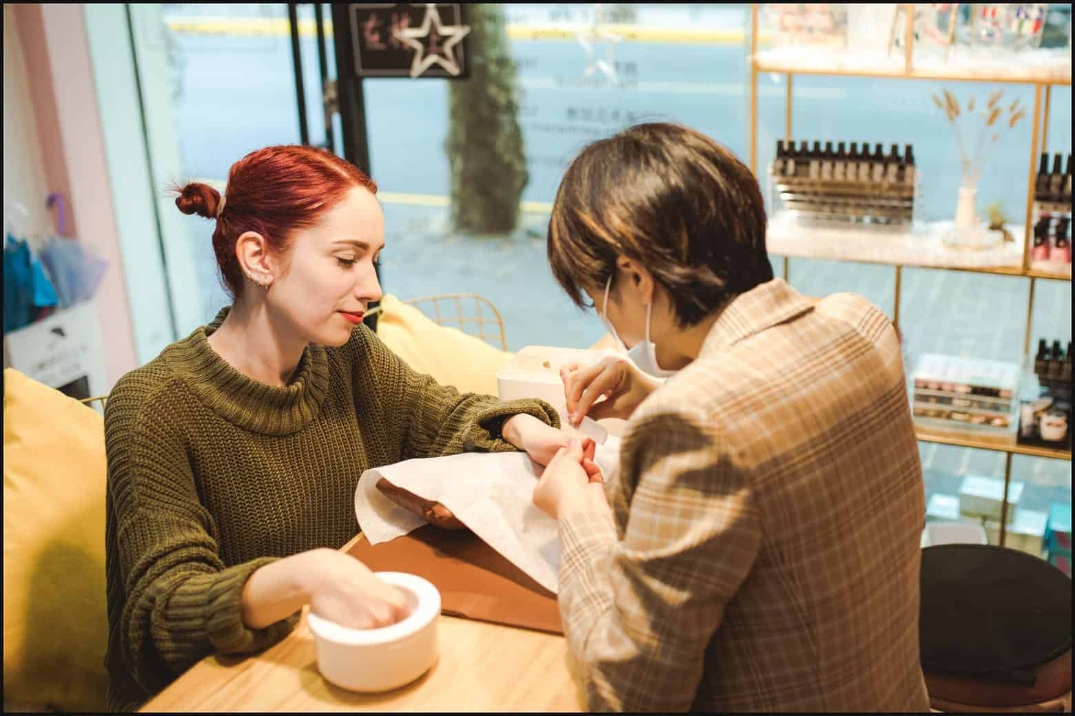 Woman wearing a blue shirt getting her nails painted by a nail technician