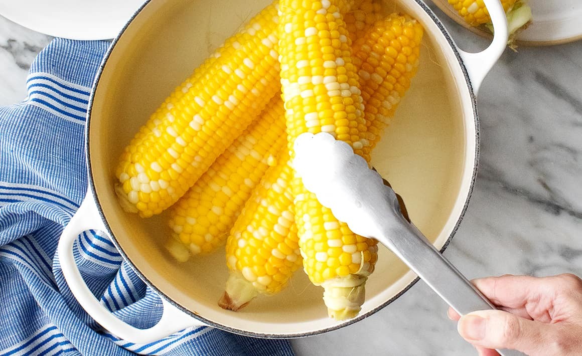 Hand removing ear of corn from pot of hot water with tongs