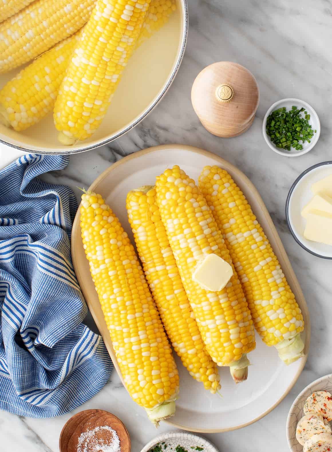 Large pot of corn next to platter of boiled corn with butter
