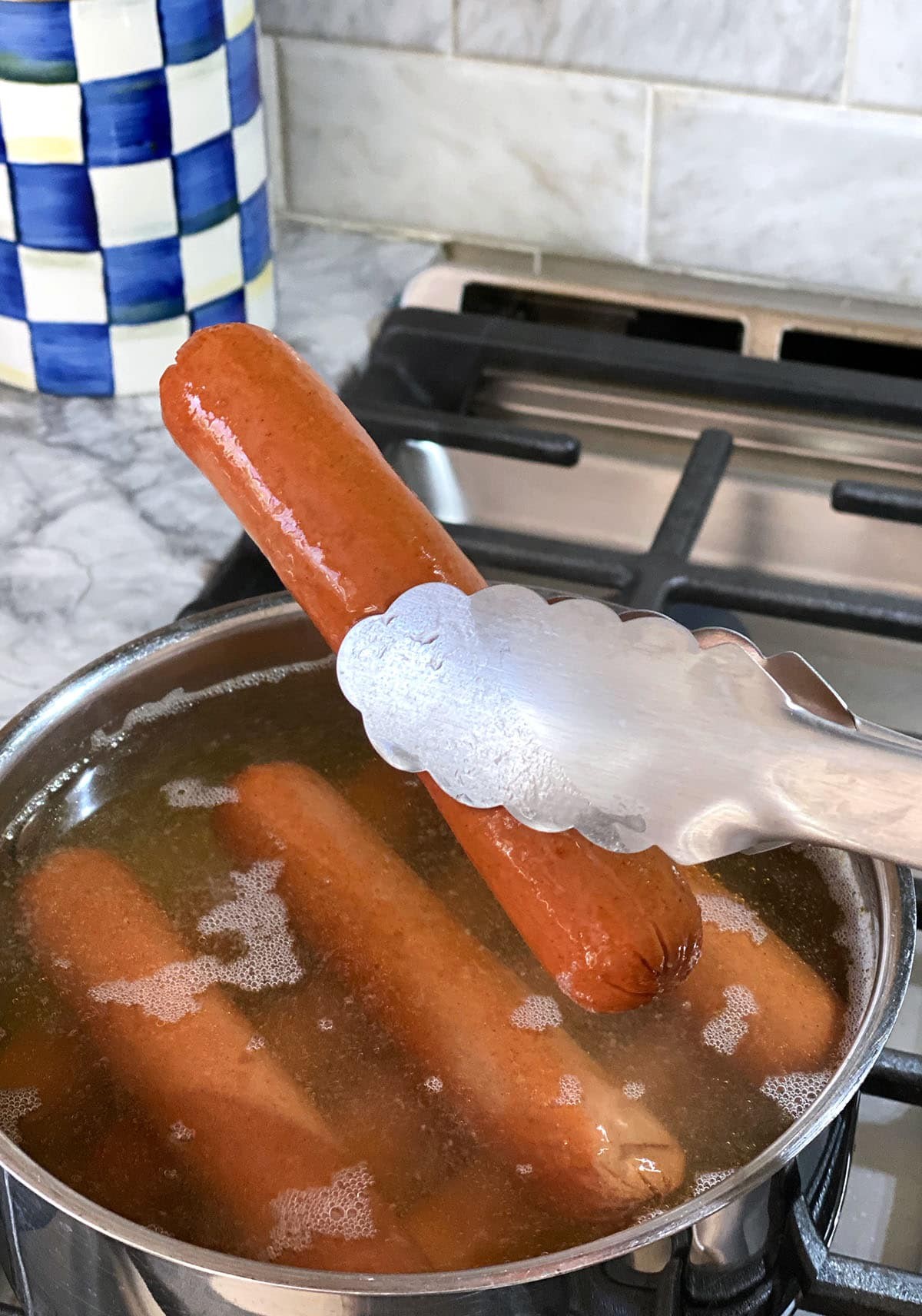 A hot dog is being lifted from a pot of boiling water with tongs.