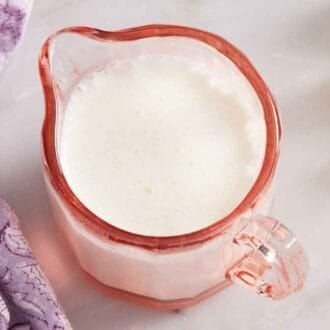 A mini pink jug of homemade heavy cream. Flowers and a purple napkin beside it