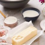 Softened butter in a bowl surrounded by baking ingredients, including flour and sugar.