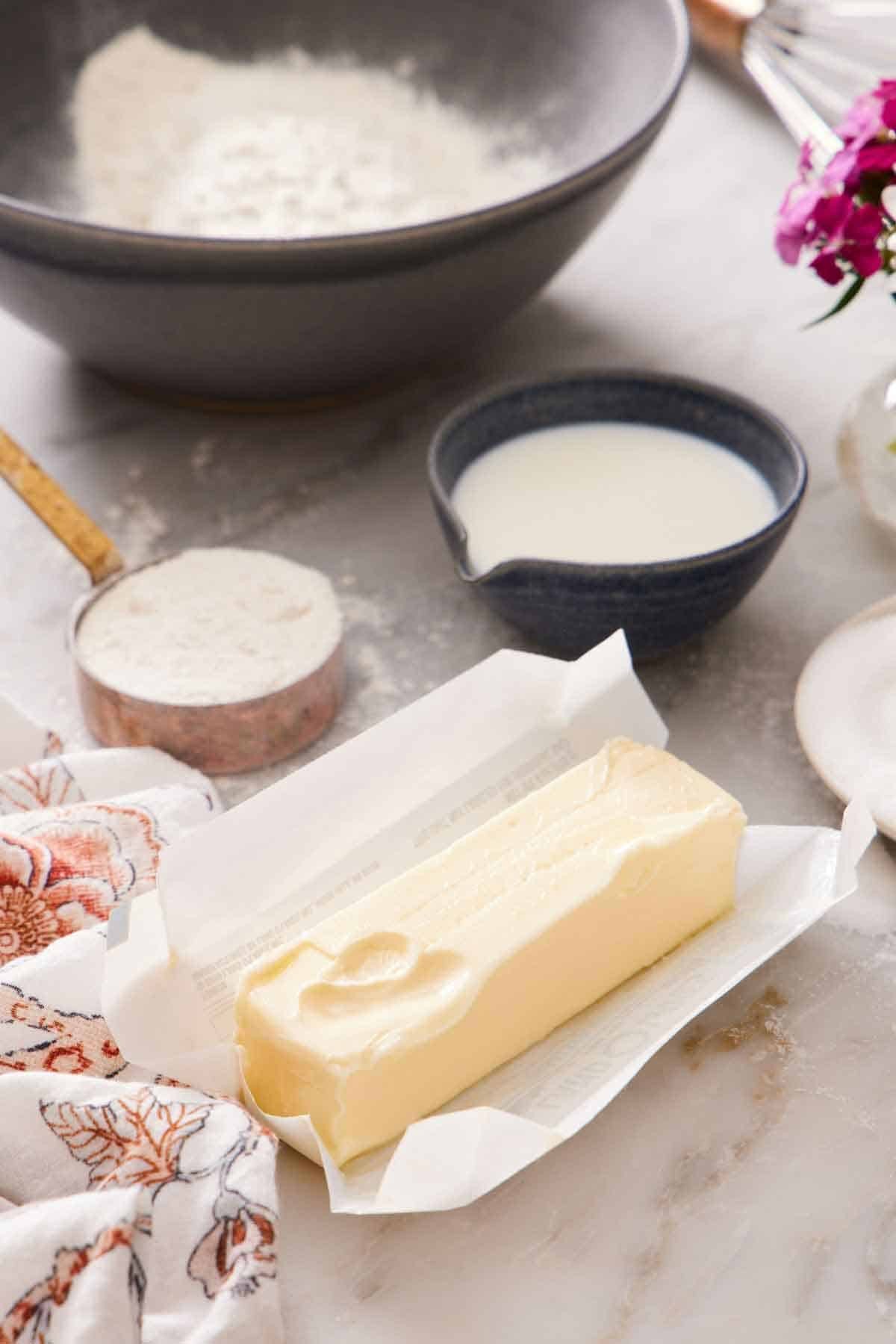 Softened butter in a bowl surrounded by baking ingredients, including flour and sugar.
