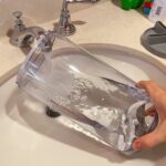 A person cleaning the humidifier tank with a brush in a sink.