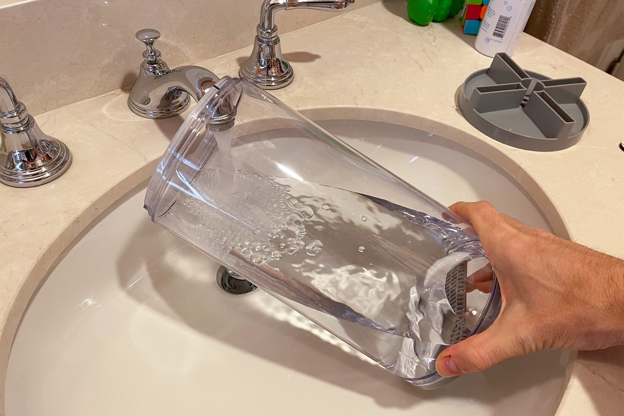 A person cleaning the humidifier tank with a brush in a sink.