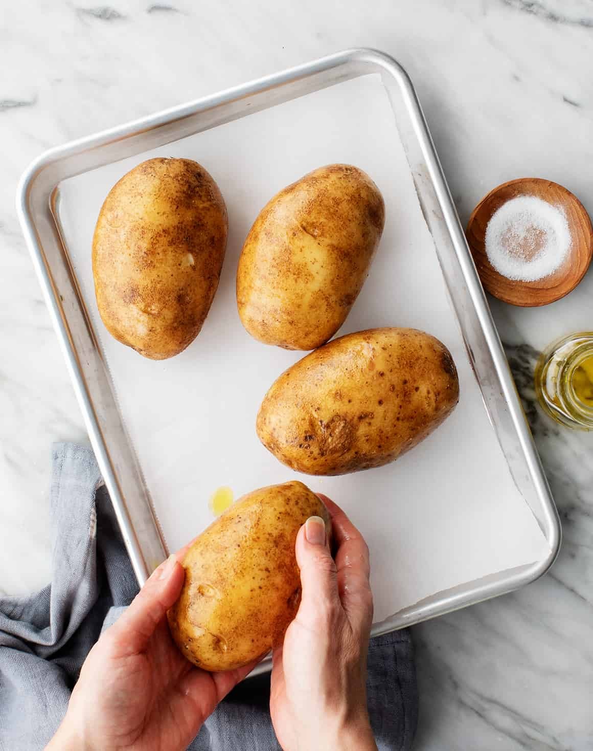 Russet potatoes being prepped for baking with olive oil and salt