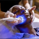 Close up on person with eyes closed getting a laser facial, gloved hands are holding their face