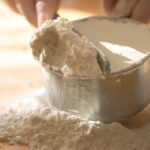 Person using measuring spoons and cups to measure baking powder.