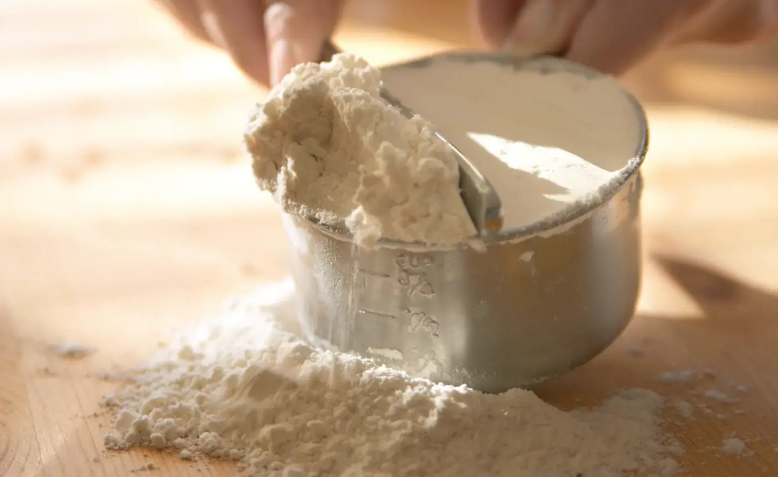 Person using measuring spoons and cups to measure baking powder.