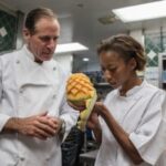 Chef preparing food in a culinary school kitchen Alt text: Chef demonstrating knife skills to a student at CASA culinary school