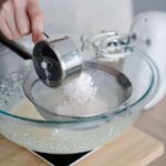 A baker's hands straining flour into a bowl for a recipe.