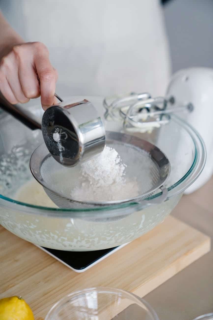 A baker's hands straining flour into a bowl for a recipe.