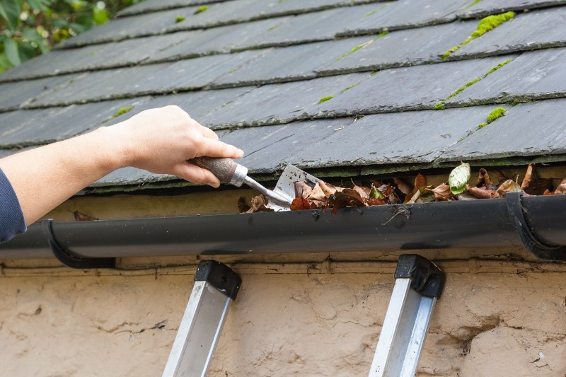 Homeowner cleaning gutters with a trowel
