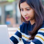 South Asian American student focused on her laptop while applying to college in an outdoor park setting