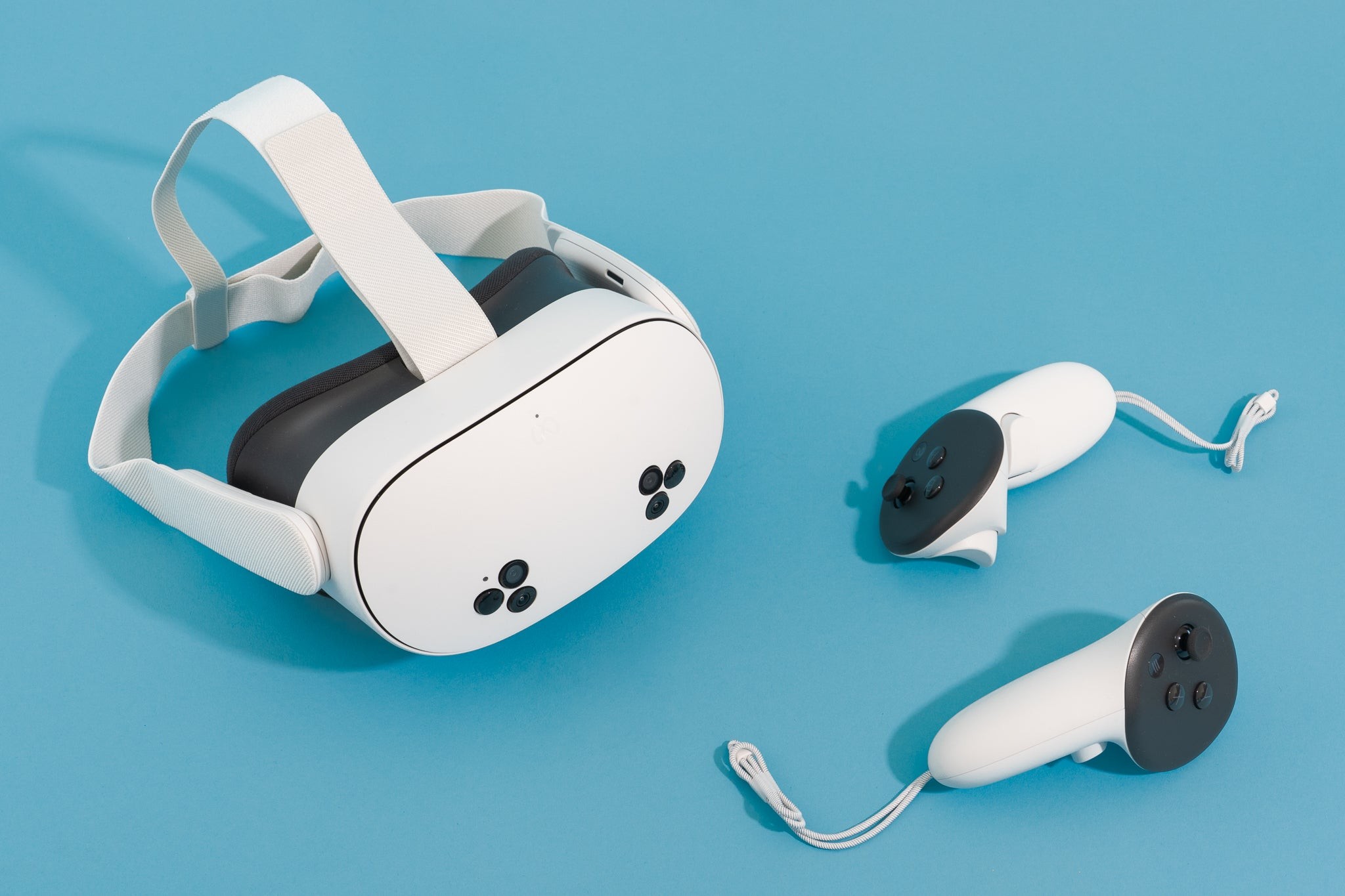 A Meta Quest 3S headset and two controllers sitting on a blue surface, highlighting its sleek design.