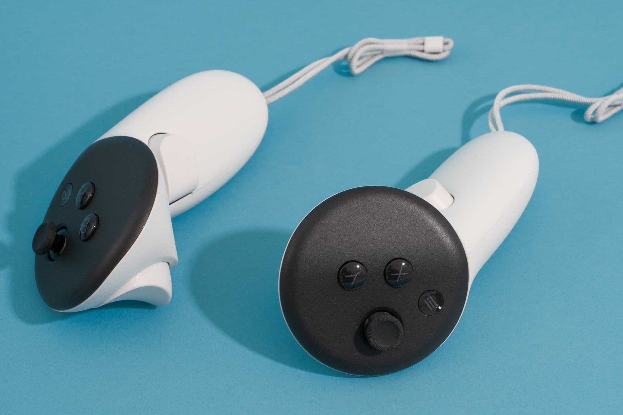 Two Meta Quest 3S controllers sitting on a blue surface, showcasing their ergonomic design.